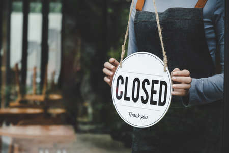 Closed. friendly waitress wearing protection face mask turning open sign board on glass door in modern cafe coffee shop, cafe restaurant, retail store, small business owner, food and drink conceptの写真素材