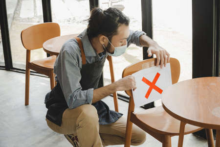 waitress service man wear protective face mask placing paper sign on seat for keep distance to protect infection coronavirus (covid-19) in cafe restaurant, new normal and social distancing conceptの写真素材