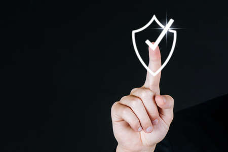 business man hand touching shield check mark icon virtual screen graphic diagram on dark background, internet security, innovation, network connection, investment and digital technology conceptの写真素材