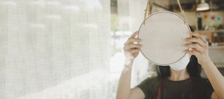 wide banner. waitress staff wearing protection face mask turning blank wooden sign board hanging on glass door in cafe restaurant, advertising, advertisement marketing and small business owner conceptの写真素材
