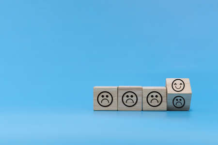 Happy and Unhappy emotion. happy smile face with sad face on wooden cube on blue background, positive think, social issues, customer satisfaction ,positive attitude, optimism and pessimism conceptの写真素材