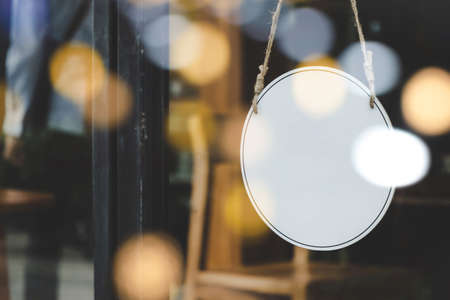 Signboard. blank vintage wooden sign board hanging on glass door with bokeh light in modern cafe restaurant, copy space for text advertising, advertisement marketing and small business owner conceptの写真素材
