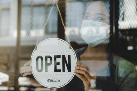 asian waitress staff woman turning open sign board on glass door with bokeh light in cafe coffee...