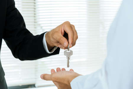 real estate broker manager giving house key to customer after signing contract for buying house in estate agent office, investment, home loan contract, selling house, real estate conceptの写真素材