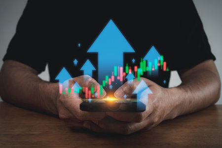 Close up of hands using smartphone with glowing upward arrows and stock market candlestick charts. Concept of financial growth, investment success, online trading, stock market and digital economy.の写真素材
