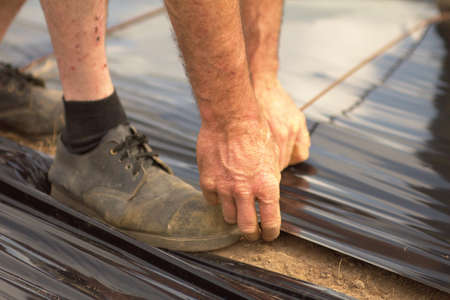 Hands of a farmer fixing a black plastic roll の写真素材