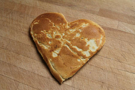 A pancake shaped as a heart, on a wooden table  A sweet way to say I love youの写真素材