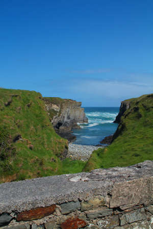 Small bay and grassy cliffs with stone fence separating the beach from the road in Ireland
の写真素材