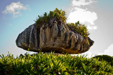Natural rock formation in unique shape on green grass against blue skyの写真素材