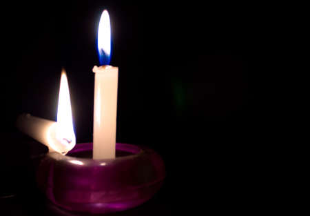 Two lit candles against black background indoors