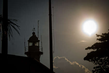 Silhouette of lighthouse light pole and tree against sunlightの写真素材