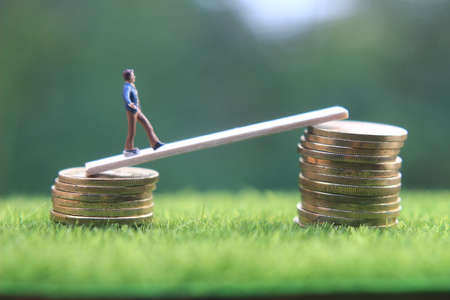 miniature figure young bussinesman keep trying to get higher income walking at stack of coin at fresh green grass in the morningの写真素材