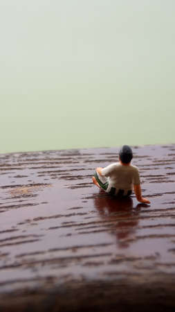 Mini figure toy old man sit at scratch wooden balcony at river side with copy or negative space for text placement areaの写真素材