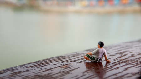 Mini figure toy old man sit at scratch wooden balcony at river side with copy or negative space for text placement areaの写真素材