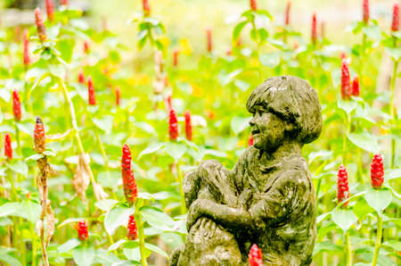 Child statue in red flowers field on green backgroundの写真素材