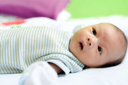 Baby lying on a bed while looking around: he want to talk with you