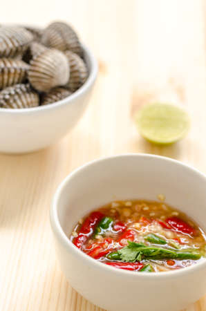 steamed blanched clams in white bowl and spicy dipping sauce on wooden backgroundの写真素材