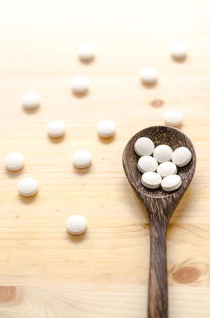 medicine tablets and wooden spoon on wood backgroundの写真素材