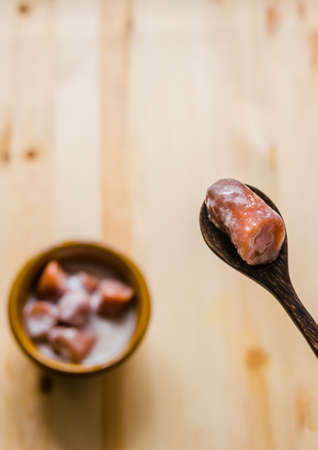 Close up on wooden spoon and blur banana with syrup and coconut milk in brown bowl on wooden background, Thai dessert.の写真素材