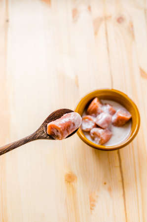 Close up on wooden spoon and blur banana with syrup and coconut milk in brown bowl on wooden background, Thai dessert.の写真素材