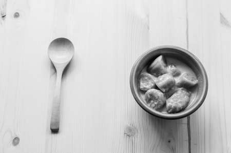 Black and white of wooden spoon and banana with syrup and coconut milk in brown bowl on wooden background, Thai dessert.の写真素材
