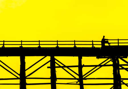 Silhouetted person sitting on the chair in bridge at sunset, Sangkla, Kanjanaburi Province, Thailandの写真素材