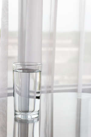 A glass of water containing fresh drinking water. Set on a table and placed in front of the curtain.の写真素材