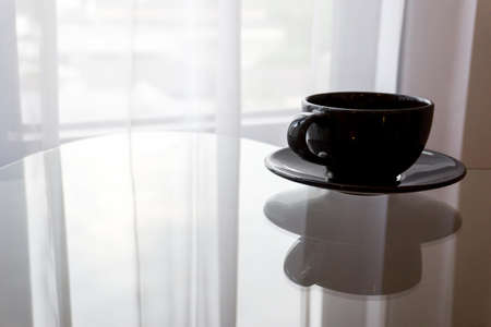 The black coffee is placed on the table in front of the curtain that blows in the morning.の写真素材