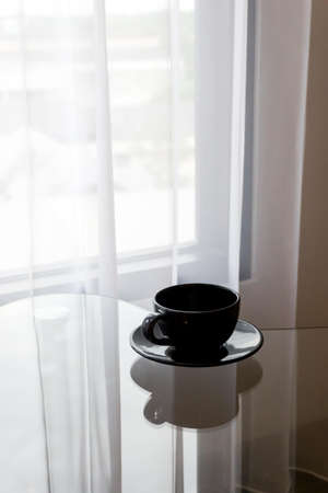 The black coffee is placed on the table in front of the curtain that blows in the morning.の写真素材