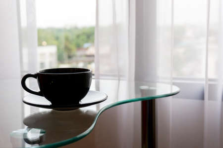 The black coffee is placed on the table in front of the curtain that blows in the morning.の写真素材