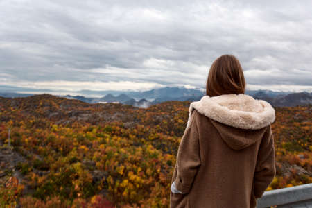Girl standing backwards and watching rainy autumn season mountain landscape with cloudy skyの写真素材