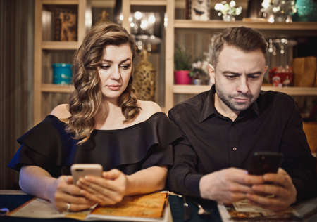 couple sitting in a restaurant waiting for an order. the girl is holding a phone and peeping a man in the phone.の写真素材
