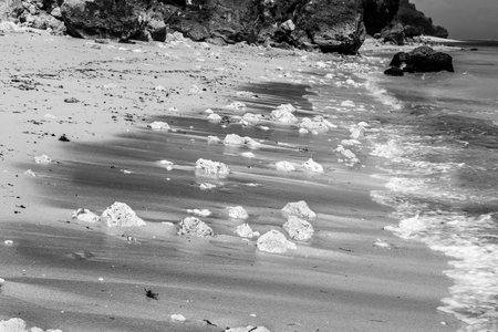White and black picture of stones and pebbles on a sandy beach with wave crashingの写真素材
