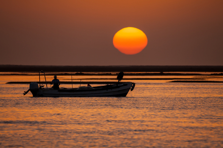 Fisherman boat at sunset with gradient colors and large sun on backgroundの写真素材