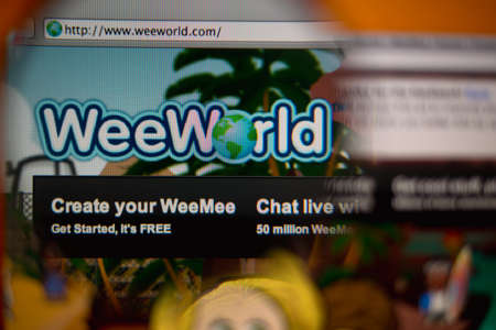LISBON, PORTUGAL - AUGUST 27, 2014: Photo of WeeWorld homepage on a monitor screen through a magnifying glass.のeditorial素材