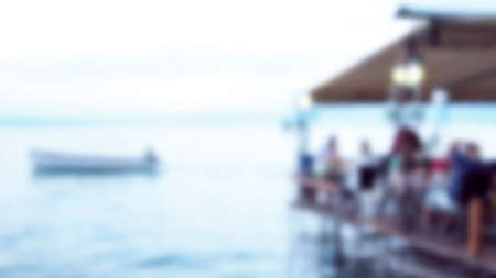 Blurred image of waterfront luxury restaurant and people at travel place with a boat sailing. Twilight blur holiday concept.の写真素材