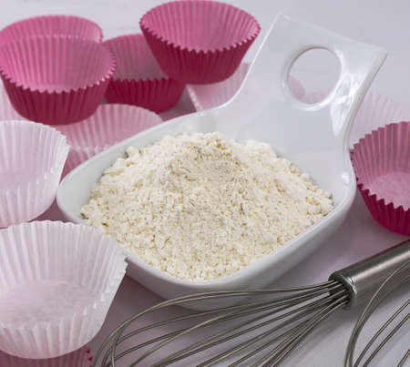 flour in a white bowl, whipping rods and paper bases for muffins on white backgroundの写真素材
