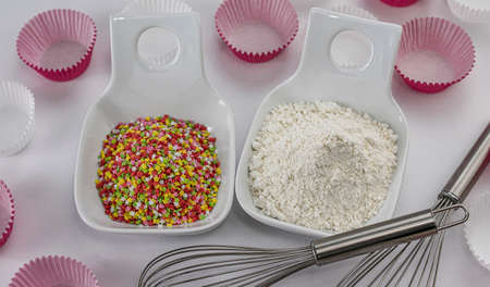 Pile of wheat flour and decorative sugar stars in two bowls with rods to beat eggs and white and pink paper molds for muffinsの写真素材