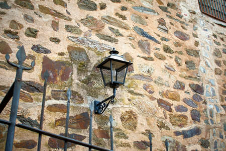 Stone facade with a black cast iron lantern for outdoor lighting. Parador of Guadalupe, west of Spain.の写真素材