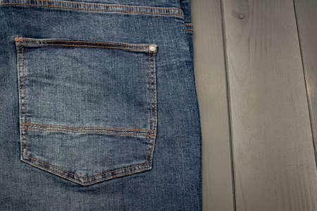 Back pocket of a washed blue denim trousers with gold stitching on gray wooden backgroundの写真素材