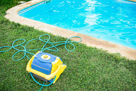 Automatic pool cleaner with electric hose protected on grass and freshly cleaned pool