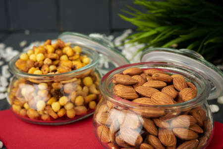 Glass jars with unpeeled natural almonds and mixed nuts such as corn, chickpeas, and raisins.