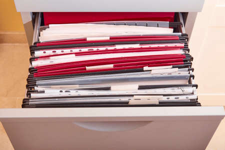 Documents organized in a metal office drawer filing cabinet full of subfolders and folders in an officeの写真素材