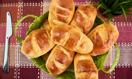 milk bread buns in a wicker basket on a red and white checkered tablecloth with a plant and a knife