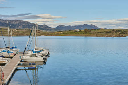 Boats moored in a small marina with calm waters and mountains in the backgroundの写真素材