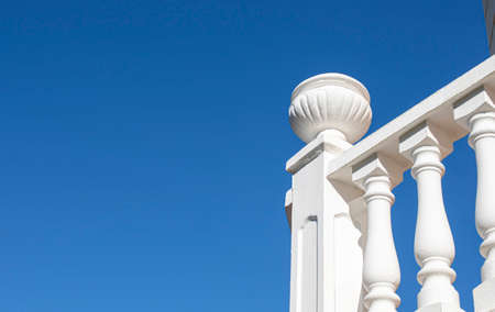 Sun-drenched white balustrade on blue sky background. Pillar finished with decorative planter made of concreteの写真素材
