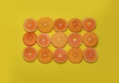 Slices of persimmons and tangerines on a yellow background.の写真素材