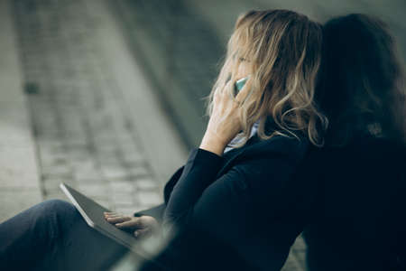 Business woman with smartphone in the hand and laptop on knees.の写真素材
