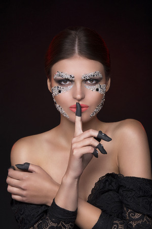 Beautiful sensual woman looking at camera with face-art make-up and showing silence gestureの写真素材