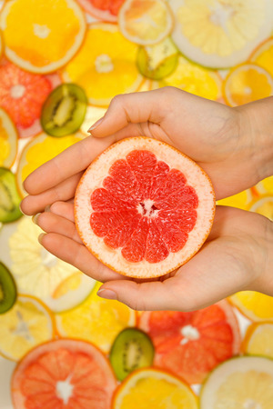 Woman holding grapefruit slice in the hands on fruits backgroundの写真素材